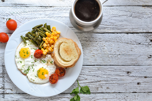 Fried eggs with tomatoes, green beans, corn and toast. English vegetarian breakfast. Coffee and fried eggs. Light wooden background. Top view. Free space for text.