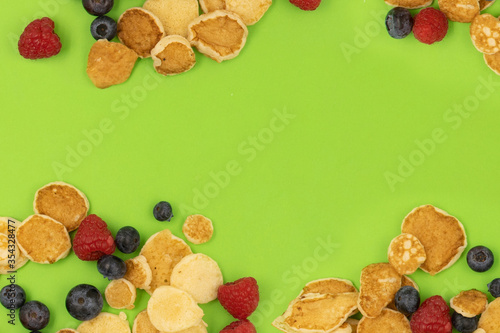 A bowl with mini pancake cerea on green background. Trendy food. Tiny cereal pancakes with blueberries and raspberries. Copy space