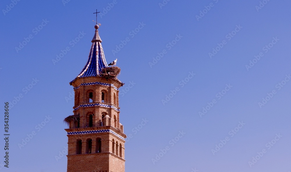 Dome of the catholic church made of red brick and decorated with blue and white ceramic tiles. Stork nests on top. Tauste, Zaragoza province, Aragon, Spain