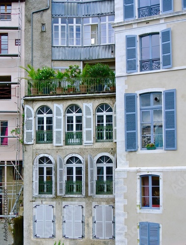 Facades of buildings in the city. High floor windows with pastel blue shutters, balconies with outdoor plants. Typical french houses. Pau, France