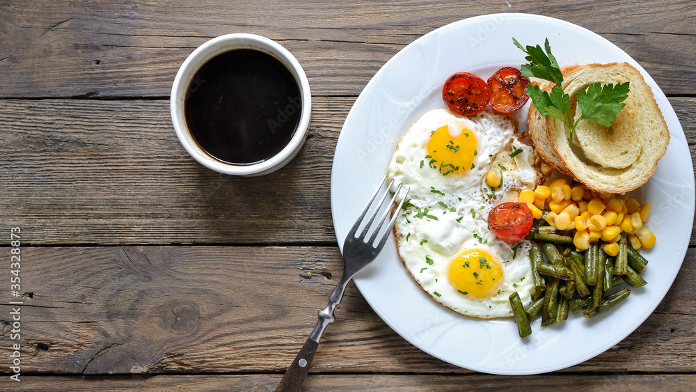 Fried eggs with tomatoes, green beans, corn and toast. English vegetarian breakfast. Top view. Coffee and fried eggs on a wooden tray. Wood background. Free space for text.