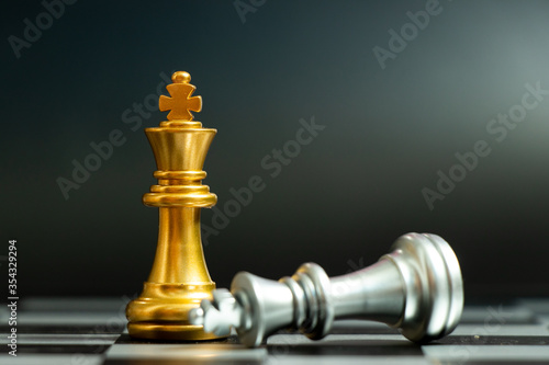 Gold king chess piece win over lying down silver king on black background