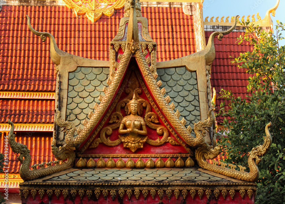 Obraz premium Colorful roof top religious architecture showing a praying buddha image at a temple site in Siamese Lao PDR, Southeast Asia