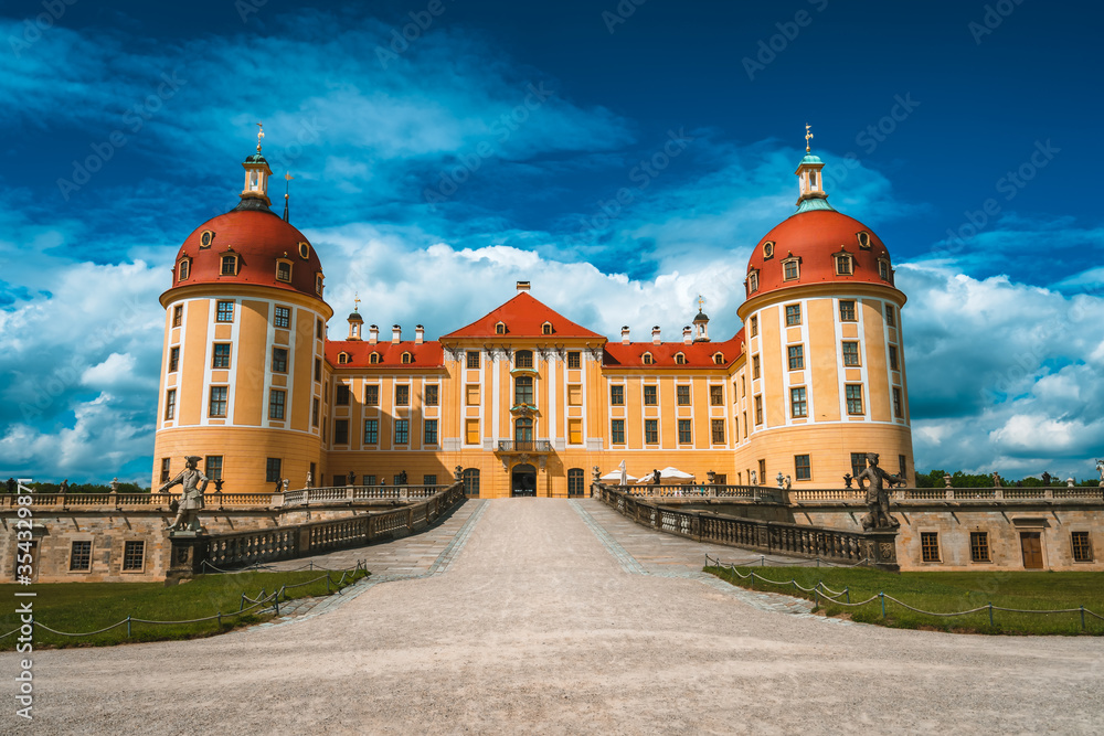 Yellow Facade of Castle Moritzburg with orange roof, Saxony, Dresden, Germany. Beautiful spring day with blue sky and white clouds. Surrounded by beautiful park