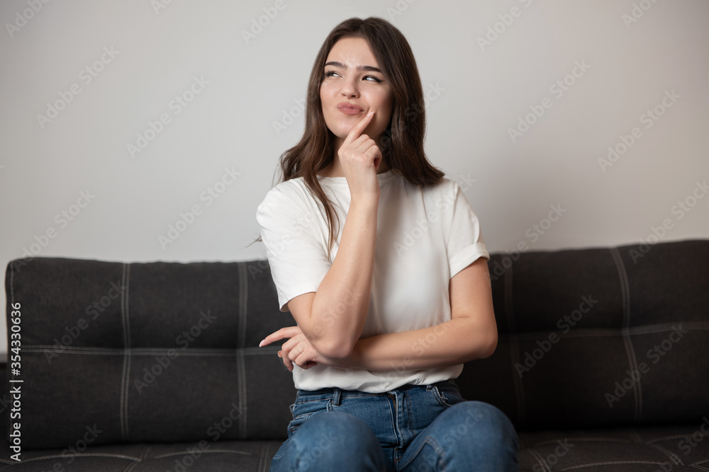 portrait of young beautiful sexy brunette woman sitting on the sofa in her appartment holding hand near face looking tricky, feels cozy at home portrait of young beautiful sexy brunette woman sitting on the sofa in her appartment holding hand near face looking tricky, feels cozy at home