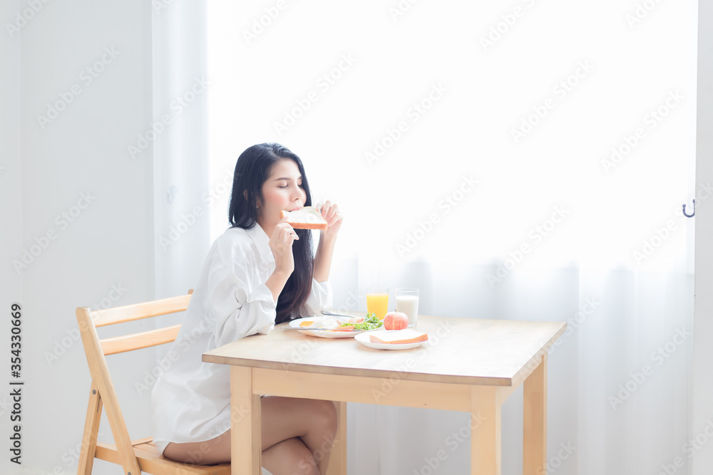 A beautiful Asian woman, Thai, is wearing a white pajamas. She is having a delicious breakfast at the dining table in the bedroom in the morning. A beautiful Asian woman, Thai, is wearing a white pajamas. She is having a delicious breakfast at the dining table in the bedroom in the morning.