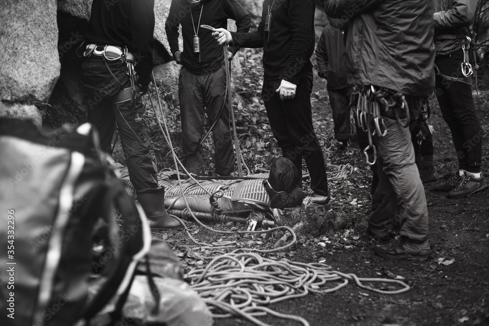 Group of rock climbers and the body of the injured laid on a stretcher for transportation, during rescue operation, black and white.