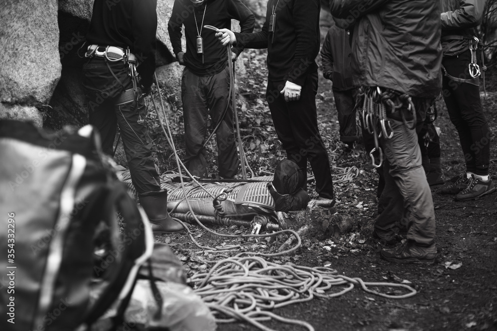 Group of rock climbers and the body of the injured laid on a stretcher for transportation, during rescue operation, black and white. Group of rock climbers and the body of the injured laid on a stretcher for transportation, during rescue operation, black and white.