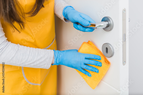 Close up of woman with surgical gloves cleaning door. Coronavirus prevention concept.