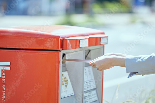 郵便ポストに封筒を入れる若い女性の手元 photo