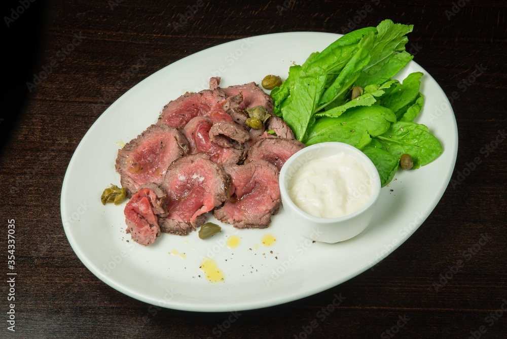 Roast beef with lettuce and garlic sauce.On a white plate. On black background