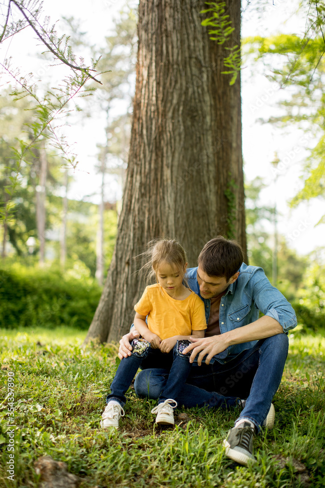 Single father sitting on grass by the tree with little daughter Single father sitting on grass by the tree with little daughter
