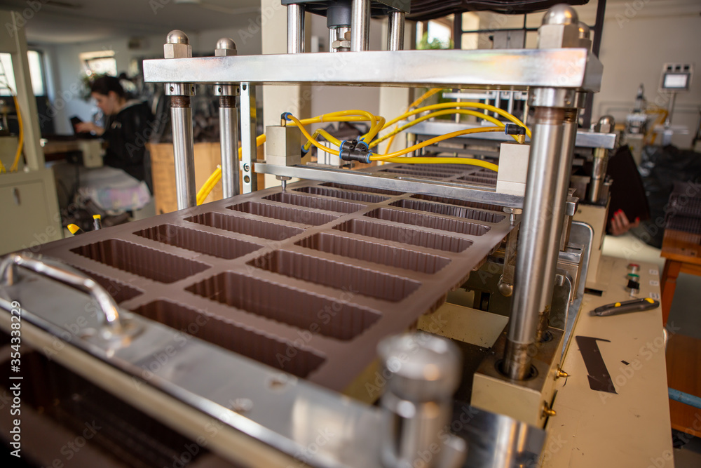 Machine for the production of plastic packaging for chocolate products. The machine has just made one board out of brown plastic. Industry. Packaging.