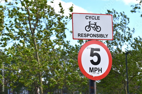 London cycle responsibly sign stating speed limit of five miles per hour positioned by a path in a park Citizens commute daily by own or rented bike or leisurely enjoy a ride around the city