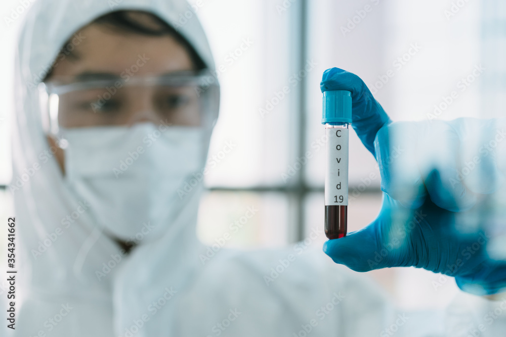 Lab Technician in Personal protective equipment PPE suit Vaccines testing of Virus Virologists are raising a tube to hold a blood sample of an infected person. Lab Technician in Personal protective equipment PPE suit Vaccines testing of Virus Virologists are raising a tube to hold a blood sample of an infected person.