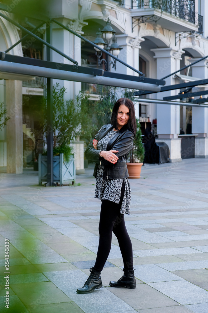 Nice, brunette woman wearing in black leather jacket walking in square city. Smile, cute lady in Batumi, Georgia. Spring time.