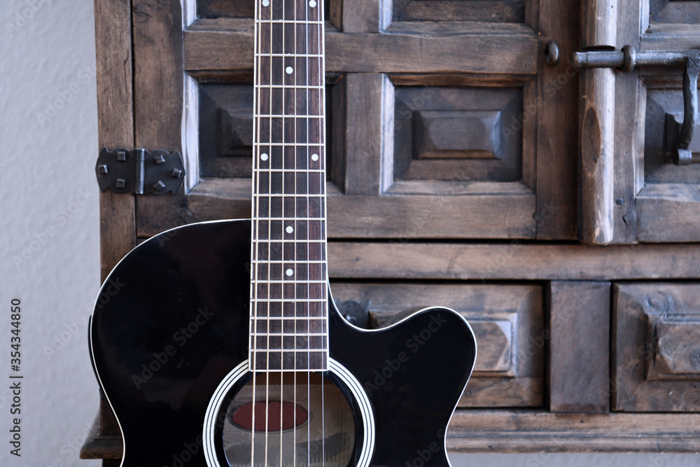 Fototapeta premium Black acoustic guitar in front of vintage wooden cupboard.