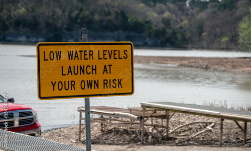 A yellow warning sign at the lake in Okalhoma gives precautions to boaters due to receeding waters. Defocused background.