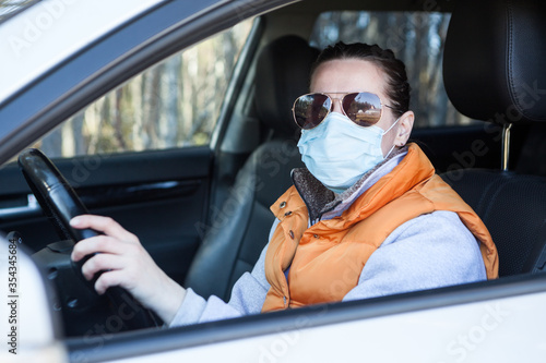 Portrait of adult woman a driver sitting in vehicle, wearing facial mask and sunglasses to prevent coronavirus infection