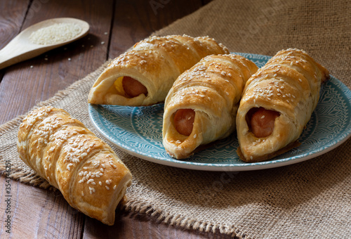 Sausage in dough sprinkled with sesame seeds on a wooden table