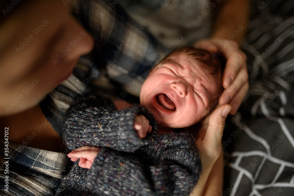 A little newborn boy in the eighth month, lies in the hands of caring parents. The boy is crying.
