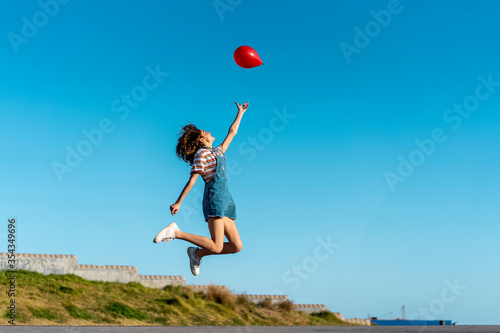 Jumping young woman, letting go of a red ballon photo