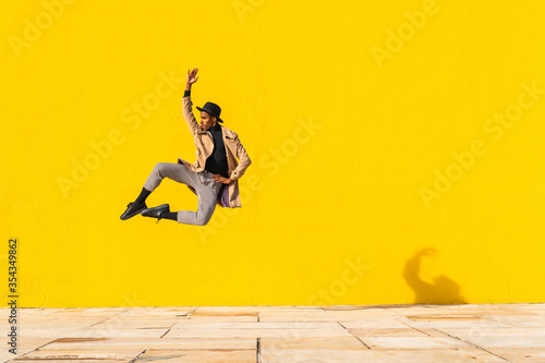 Young man dancing in front of yellow wall, jumping mid air
