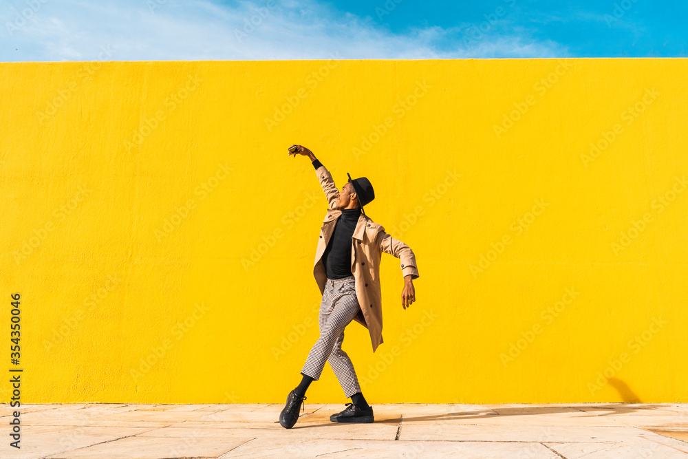 © VISTA by Westend61 - Young man dancing in front of yellow wall, taking selfies