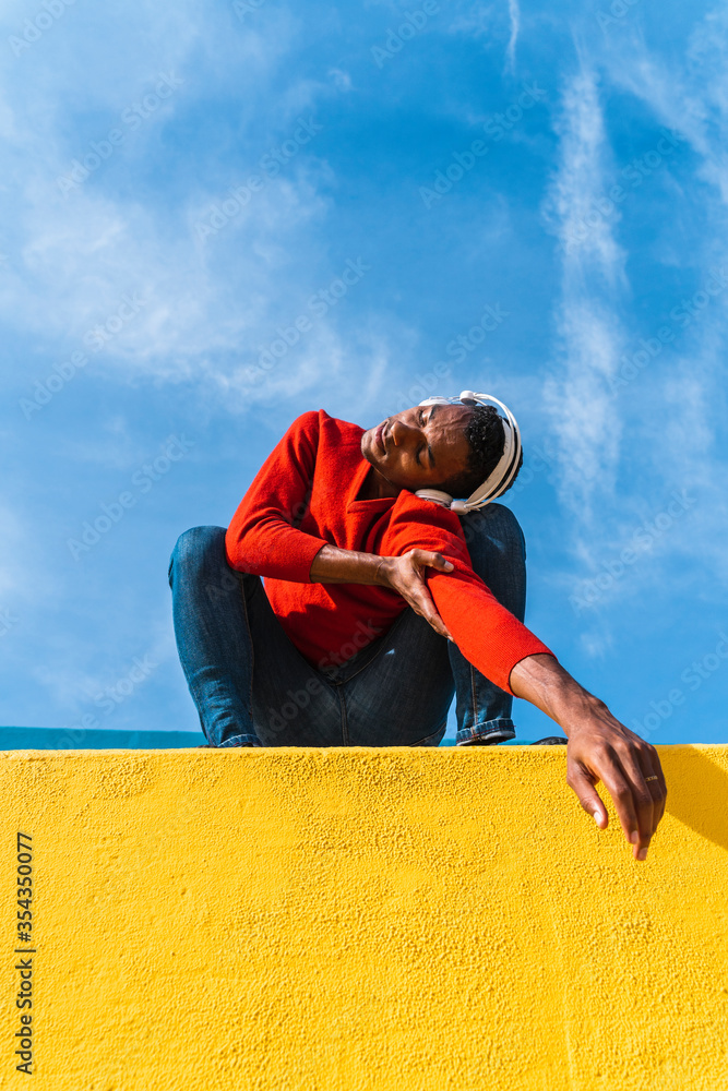 © VISTA by Westend61 - Young man with headphones, listening music, dancing on yellow wall