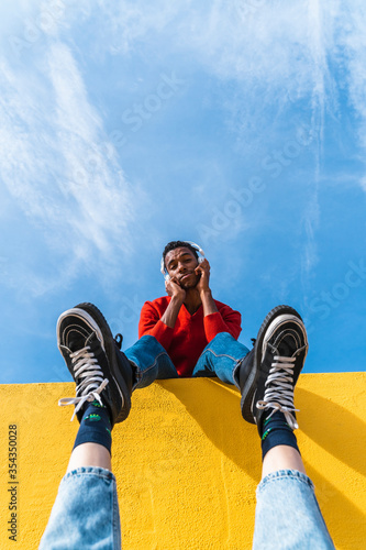 Young man with headphones, dancing for person, leaning on yellow wall photo