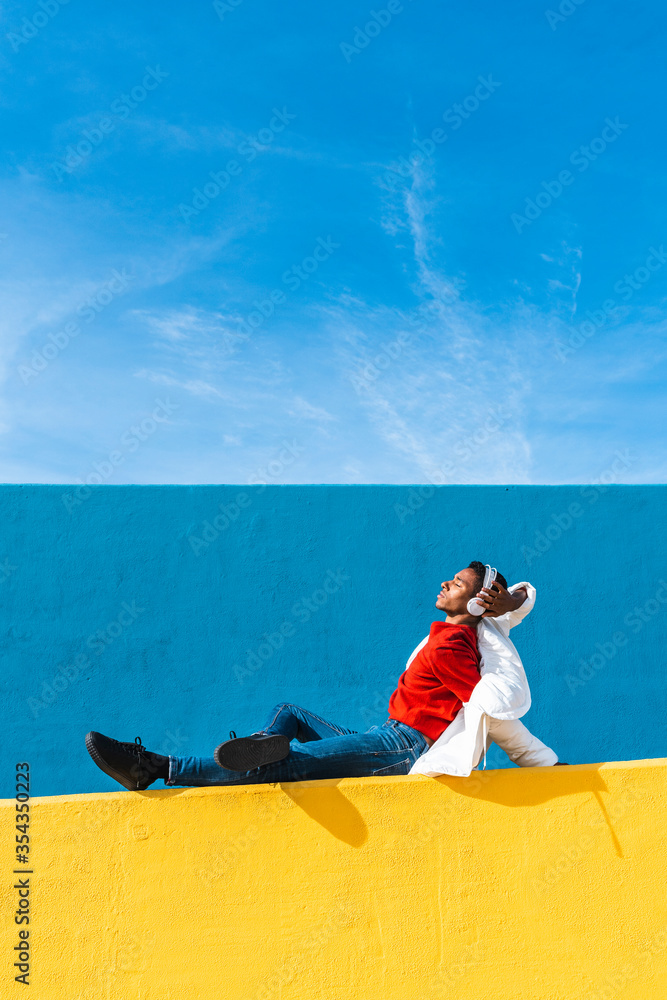 © VISTA by Westend61 - Young dancer sitting on yellow wall, listening music