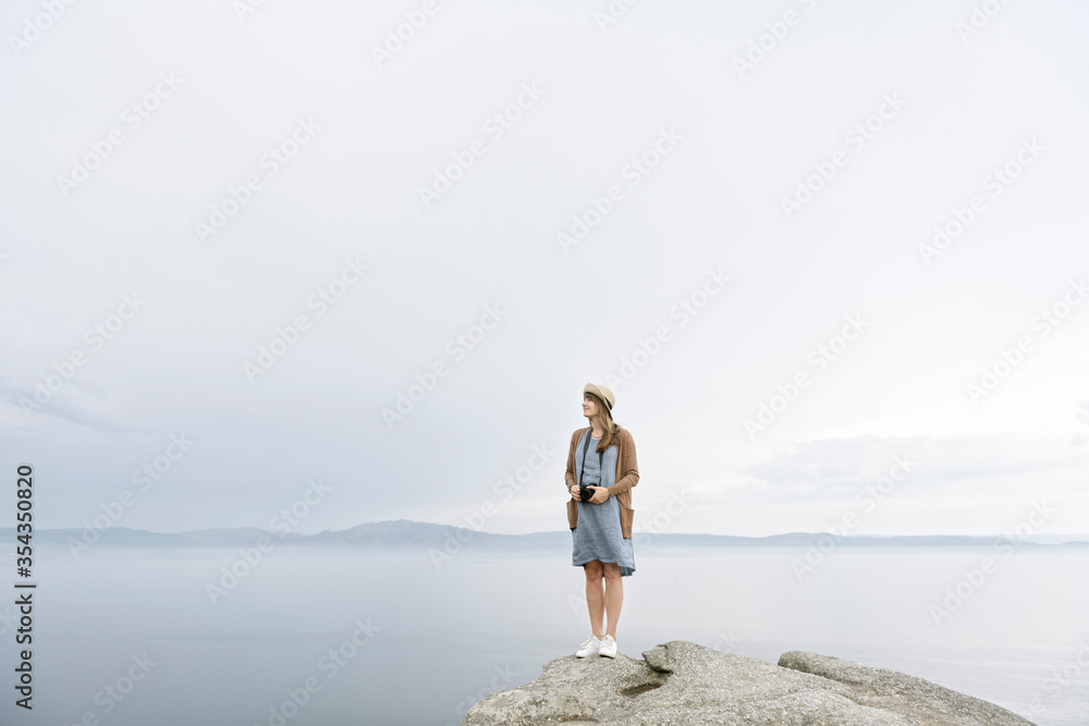Woman with camera standing on rock, looking at the sea Woman with camera standing on rock, looking at the sea