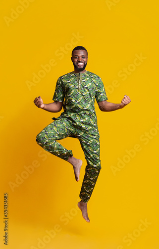 Cheerful african guy celebrating success, jumping up over yellow