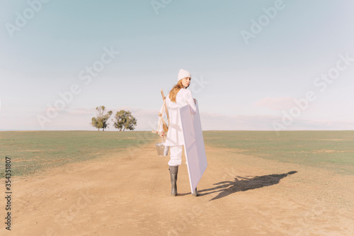 Young woman carrying easel and empty canvas on dry field photo