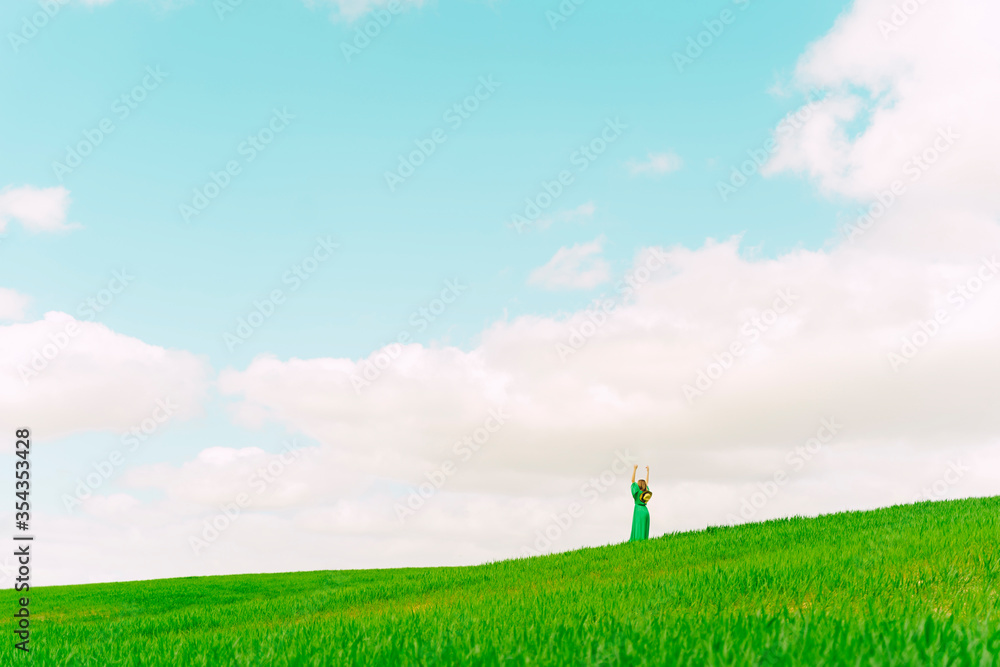 Back view of woman wearing green dress standing on a field with hands raised Back view of woman wearing green dress standing on a field with hands raised