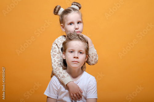 boy hugs a girl,  brother and sister on yellow background