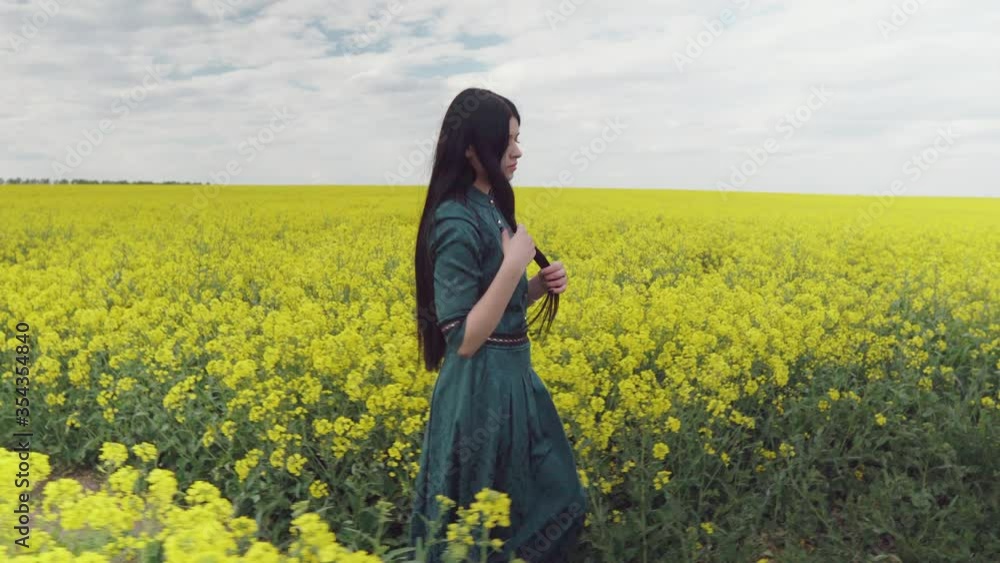 A woman walks through a flowering rapeseed field. He touches his hair and thinks about something. A woman walks through a flowering rapeseed field. He touches his hair and thinks about something.