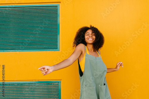 Portrait of happy young woman wearing overalls in front of yellow wall photo