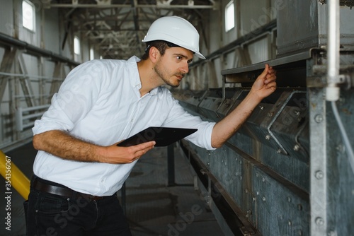 Close up of young Caucasian smiling worker with helmet on head using tablet for work while standing in warehouse.