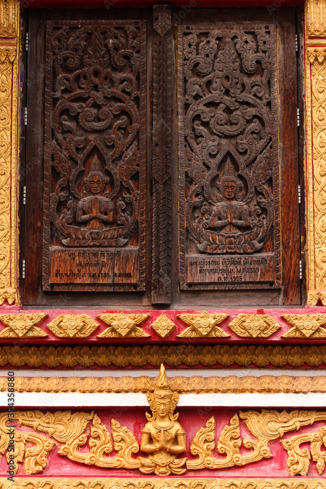 Praying buddha image as wood carving on a window in a temple and religious site in Siamese Lao PDR, Southeast Asia
