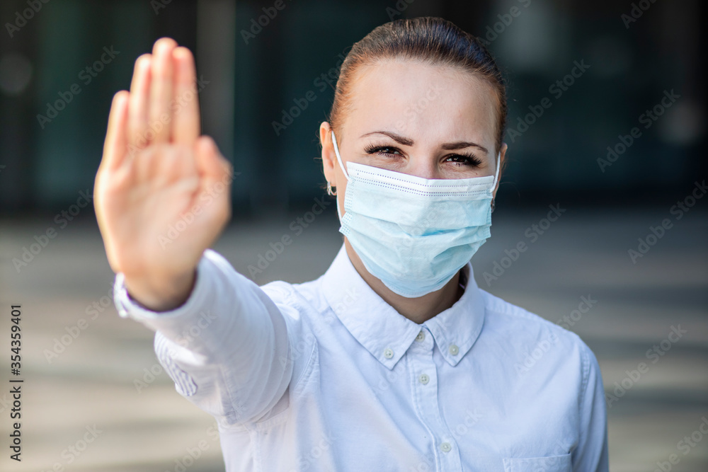 Girl, young woman, businesswoman in protective sterile medical mask on face look at camera outdoors office, show palm, hand, stop no sign. Air pollution, virus, pandemic coronavirus concept. Covid-19 Girl, young woman, businesswoman in protective sterile medical mask on face look at camera outdoors office, show palm, hand, stop no sign. Air pollution, virus, pandemic coronavirus concept. Covid-19