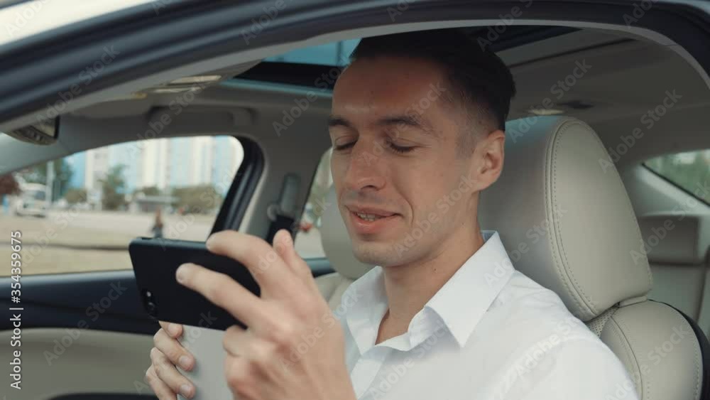 Portrait young man businessman sitting in a car, drinking coffee and watching funny videos on a smartphone. Portrait young man businessman sitting in a car, drinking coffee and watching funny videos on a smartphone.