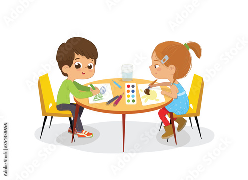 Boy and Girl sit at the round table and draw picture with watercolor and pencils. Drawing activity in the art class. Boy and Girl Draw Pictures with paints and pencils. 