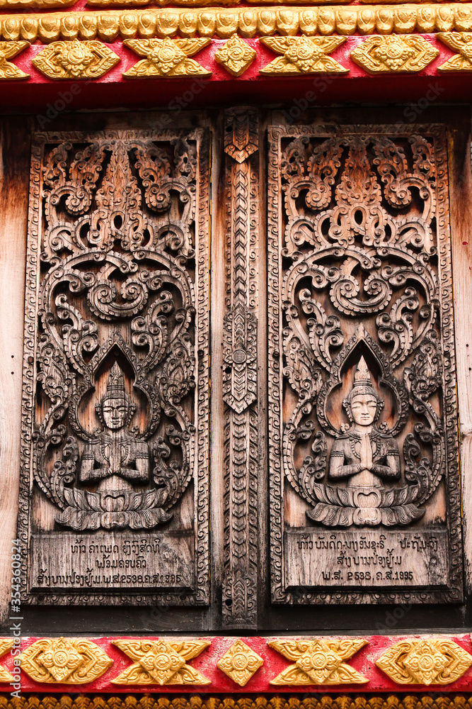 Entrance door with wooden carvings of religious buddha images in a temple in Siamese Lao PDR, Southeast Asia