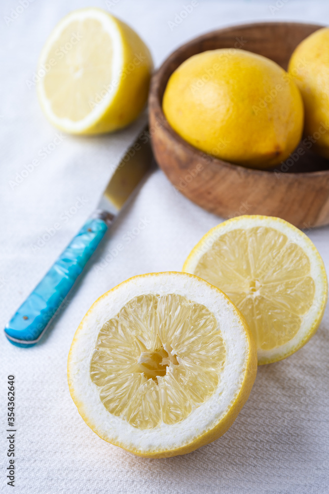 Aerial view of half lemons, blue knife and wooden bowl, on white dishcloth, selective focus, vertical Aerial view of half lemons, blue knife and wooden bowl, on white dishcloth, selective focus, vertical