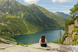 Tourist woman in the mountains looking at lake Morskie Oko. Back view. Adventures in the high mountains. Girl hiking the Tatra National Park, Zakopane, Poland. Carpathian mountains on background.