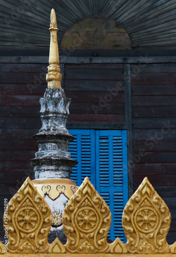 Tip of a stony and golden painted stupa in front of a religious wooden monks building or home in Siamese Lao PDR, Southeast Asia