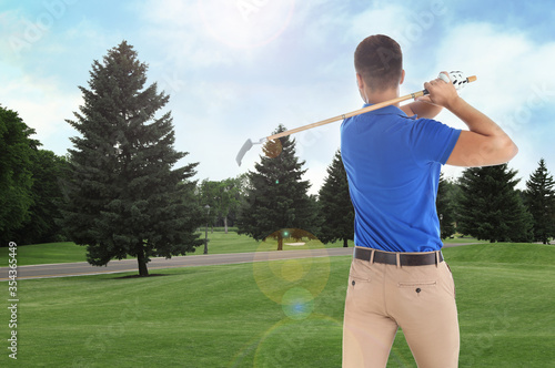 Young man playing golf on course with green grass, back view. Space for design