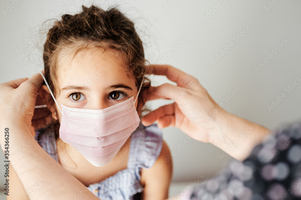 Girl with coronavirus mask prepared to go outside. Mother's hands putting the mask on her girl to prevent contagion Girl with coronavirus mask prepared to go outside. Mother's hands putting the mask on her girl to prevent contagion