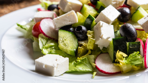 A close up of a white plate of freshly prepared Greek style salad.  Vegetables, olives, feta cheese with out dressing.